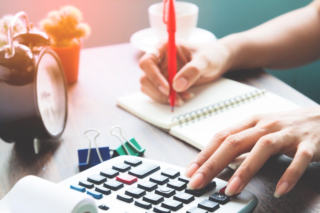 pessoa calculando imposto de renda 2024 usando calculadora caderno e lápis com relogio na mesa
