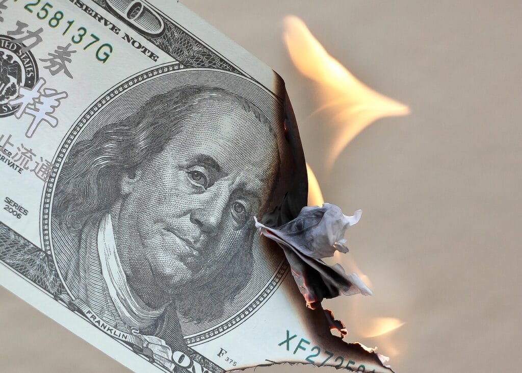 Nota de dólar sendo queimada representa desperdícios financeiros que podem ser evitados.